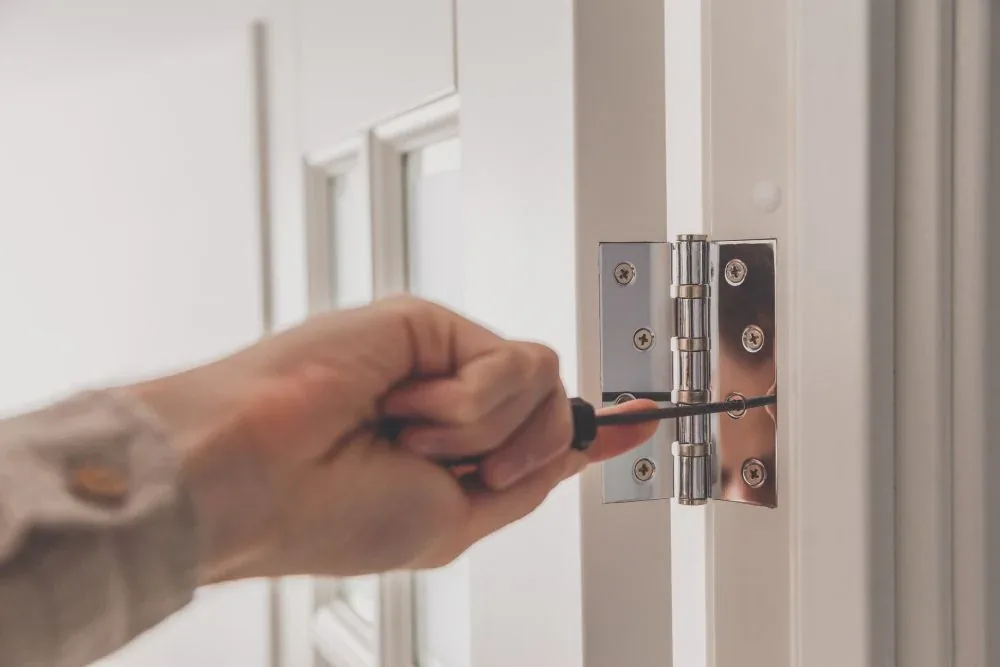 Installing a polished stainless steel door hinge with a screwdriver on a white interior door